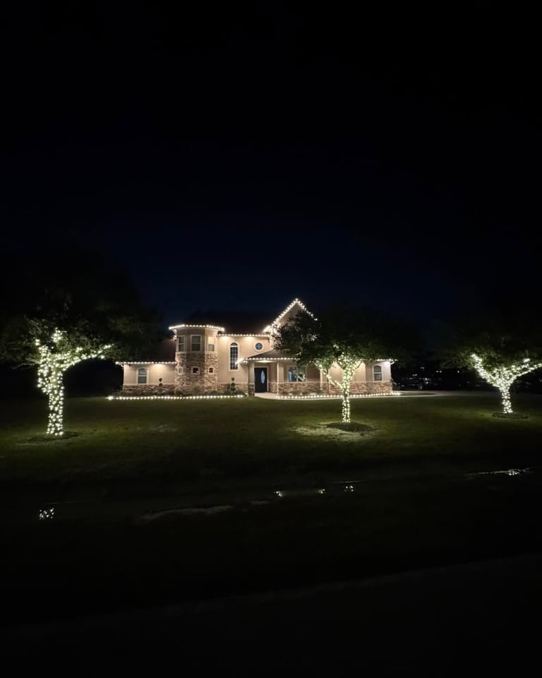 Beige stone two-story home with Christmas lights on rooflines and lit trees, installed by OnSite Pros in Greater Houston