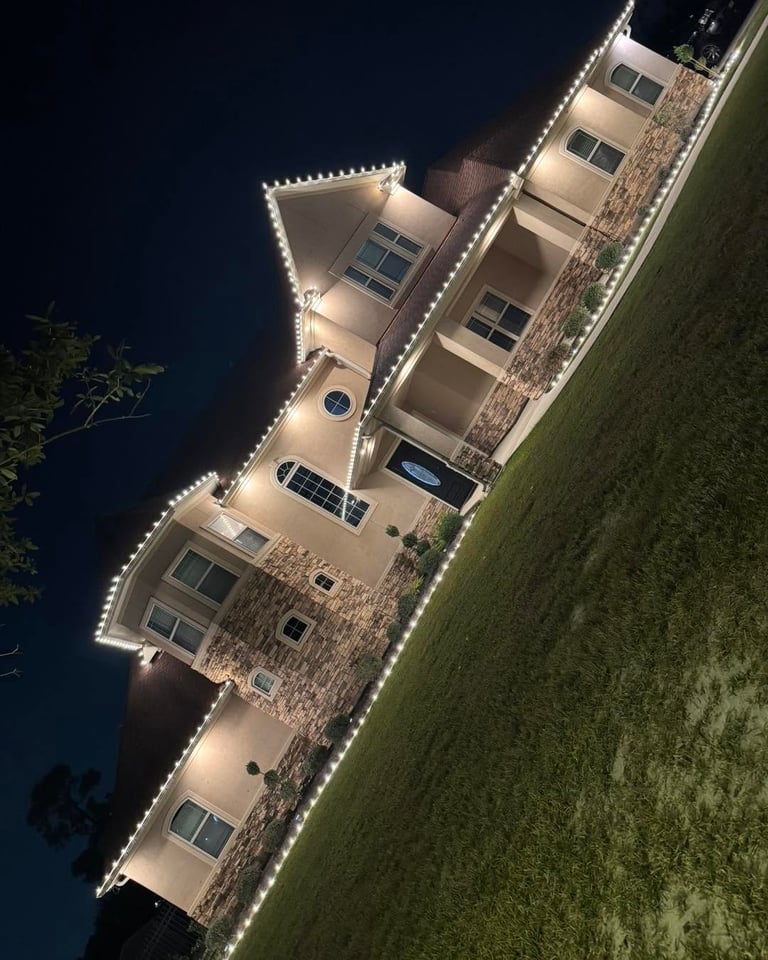Beige stone two-story home with Christmas lights on rooflines and lit trees, installed by OnSite Pros in Greater Houston